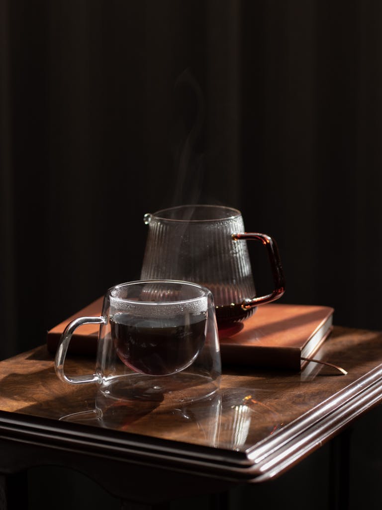 Glass coffee cup and a pot with steam rising on a wooden table, exuding warmth and elegance.